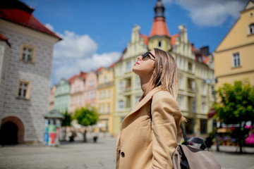 Woman in sunglasses and backpack in aged city center square. Poland