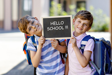 Two little kid boys with backpack or satchel. Schoolkids on the way to school. Healthy children, brothers and best friends outdoors on street. Hello school on chalk desk. Happy siblings