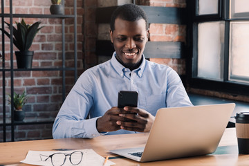 African american smiling businessman sitting at table with laptop and smartphone