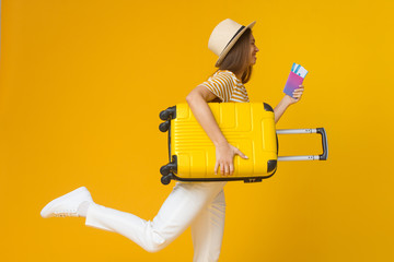 Young woman hurrying up for plane with suitcase and air tickets in hands, isolated on yellow background