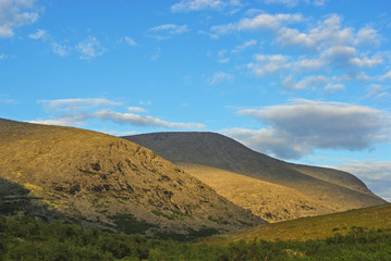 Fototapeta na wymiar Khibiny. Soft golden ridges of the northern mountains, illuminated by the setting sun and light clouds in the blue sky