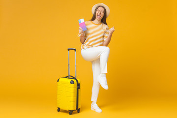 Good-looking girl feeling joy of buying tickets for vacation, isolated on yellow background