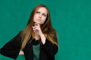 Concept close-up portrait of a pretty girl, a young woman with long beautiful brown hair and in a black jacket on a green background. In the studio in different poses showing emotions.