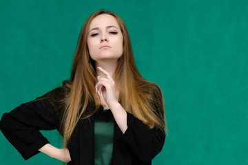 Concept close-up portrait of a pretty girl, a young woman with long beautiful brown hair and in a black jacket on a green background. In the studio in different poses showing emotions.