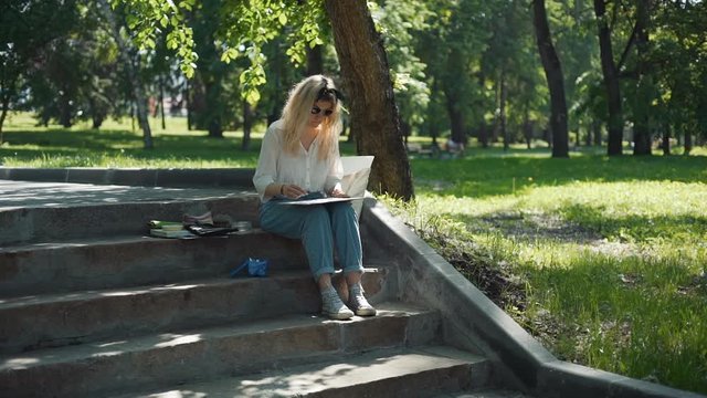 Professional Painter Working in a City Park in Sunny Summer Day while Sitting on Steps. Female Street Artist Doing a Sketch for Future Picture Outdoors. Creativity Inspiration Expression Concept