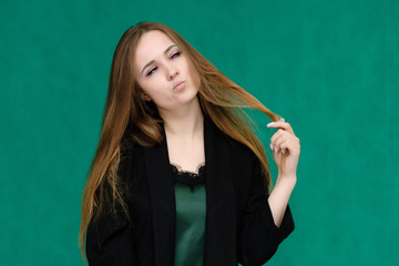 Concept close-up portrait of a pretty girl, a young woman with long beautiful brown hair and in a black jacket on a green background. In the studio in different poses showing emotions.