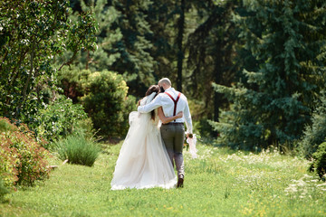 Happy bride and groom hugging and walking in garden on wedding day. Wedding couple in love,...