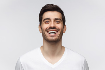 Joyful young man in casual t-shirt smiles broadly, laughing, showing perfect white teeth. Laughing out loud.