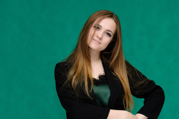 Concept close-up portrait of a pretty girl, a young woman with long beautiful brown hair and in a black jacket on a green background. In the studio in different poses showing emotions.