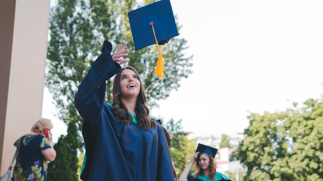 University graduates  throwing graduation hats in the air. Group of happy graduates in academic dresses near university building.
