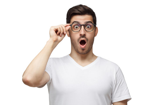 Young man shouting OMG with open mouth, surprised by low price and sales, holding glasses, isolated on white background