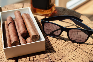 Cuban cigars in box, blur bottle of whisky and sun glasses on wood table background, closeup, copy...