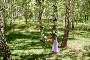 Wedding swing decorated with rose flowers hanging on tree in garden, copy space