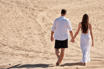 Happy loving couple holding hands  and walking in desert, copy space. Young lovers together on sands in summer