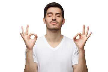 Fototapeta premium Yoga and meditation concept. Concentrated relaxed man standing with closed eyes, having relaxation while meditating, trying to find balance and harmony isolated on white