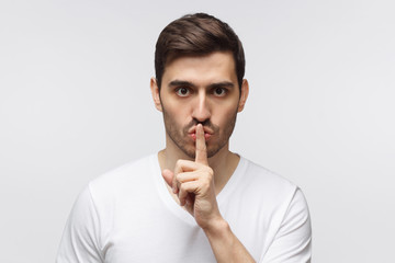Young man with shh gesture, asking for silence or to be quiet, isolated on gray background