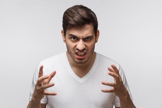 Mad young man bite his teeth, gesturing with hands. Studio portrait of angry and irritated male yelling, looking crazy and full of anger