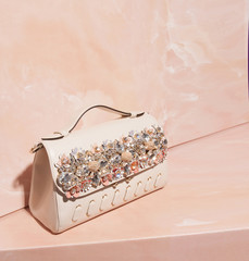 Pretty leather handbag standing on marble pink background. Crystal embellished feminine purse, coral peach pastel backdrop. Renovation concept. Fashion backlight. Copy space for your design