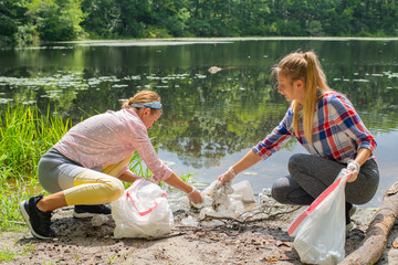 Volunteers cleaning garbage near river. Women picking up a bottle plastic in the lake, pollution and environment.