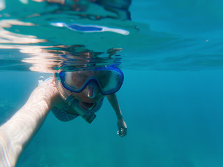 woman taking a selfie snorkeling in clear tropical waters - active holiday