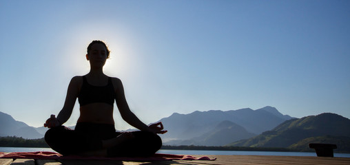 Silhouette of a woman meditating in front of sea, with mountains in background. Peaceful and healthy concept
