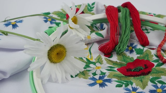 Red coral beads, embroidery hoops, embroidery thread and chamomiles on the background of white embroidered fabric