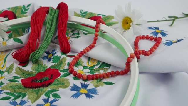 Red coral beads, embroidery hoops, embroidery thread and chamomiles on the background of white embroidered fabric