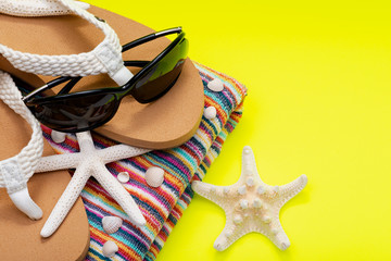 Women's Beach Flip Flops, Colorful Striped Beach Towels and black Sunglasses decorated with Starfish on yellow background as Summer Vacation Theme.