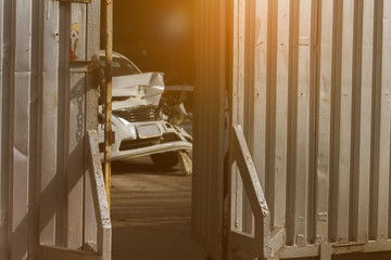 Blurred accident white car waiting for repair in the garage shop with opening strong corrugated metal sheet door and brightness radial sunlight background.