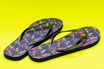 Purple Beach Day Flip Flops with dragonfly pattern isolated on bright yellow background.