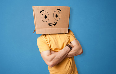 Young man standing and gesturing with a cardboard box on his head with drawn smiley face