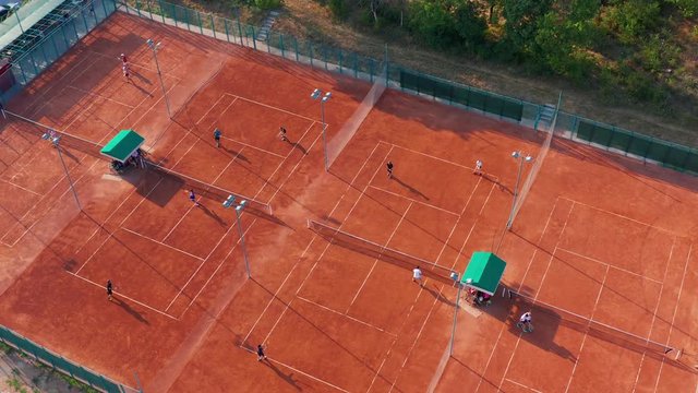 Aerial top view of unrecognizable tennis players playing tennis on the orange court on a sunny summer day.