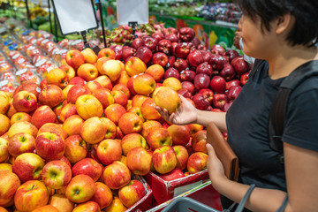 Young Asian woman buying apple at fruit stand in supermarket