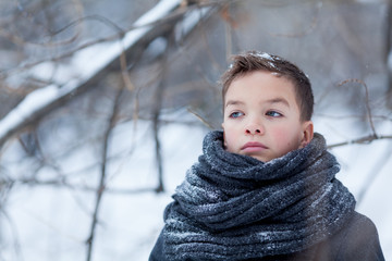 Portrait of sad boy in black coat for walk in winter park, outdoor
