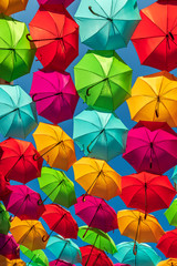 Umbrellas of various colors forming a pattern, against a blue sky.