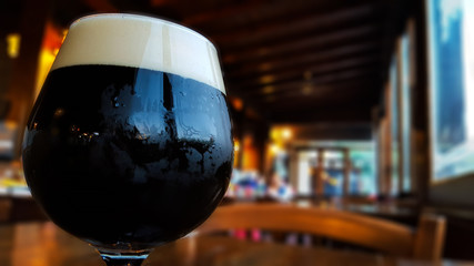 Glass of fresh dark beer on rustic pub background