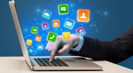 Businessman hand typing on laptop with flying application icons around