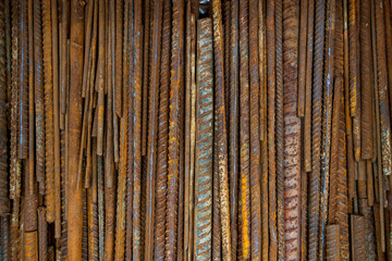 Top view stack of straight old rusty high yield stress deformed reinforcement steel or iron bars. Background vertical random pattern of deformed iron bars. 