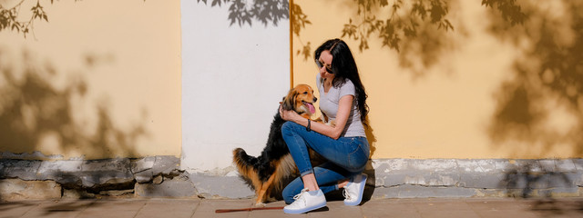 Fototapeta premium Woman and her dog on background of wall with contrast shadows. Funny spaniel mutt standing on hind paws