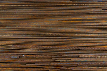 Top view stack of straight old rusty high yield stress deformed reinforcement steel or iron bars. Background horizontal random pattern of deformed iron bars. 