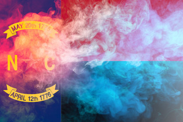 The national flag of the US state North Carolina in against a gray smoke on the day of independence in different colors of blue red and yellow. Political and religious disputes, customs and delivery.