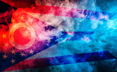 The national flag of the US state Ohio in against a gray smoke on the day of independence in different colors of blue red and yellow. Political and religious disputes, customs and delivery.