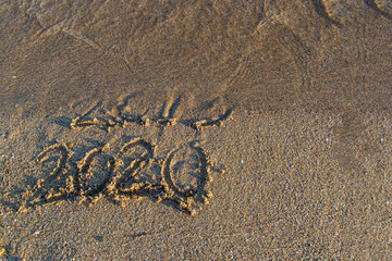 New year 2020 is coming, the inscription 2019 and 2020 beach sand, wave washes away the figures 2019. The concept leaves 2019 the year is 2020.