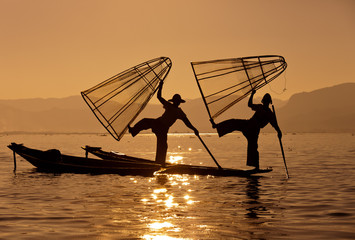Silhouette of Myanmar fisherman on wooden boat at sunset .Burmese fisherman on bamboo boat catching...