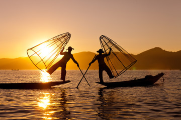 Silhouette of Myanmar fisherman on wooden boat at sunset .Burmese fisherman on bamboo boat catching...