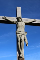 Outside life size crucifix of Jesus on wooden weathered cross on sunny day with blue sky