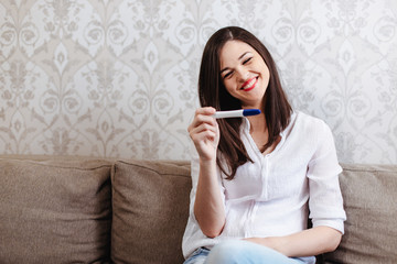 Young woman rejoices while looking at a positive pregnancy test