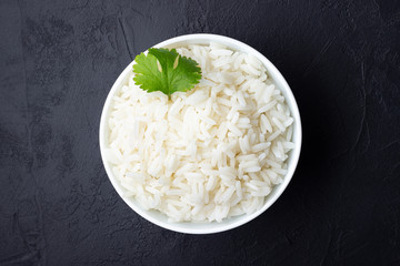 Boiled rice in a bowl on black stone background.