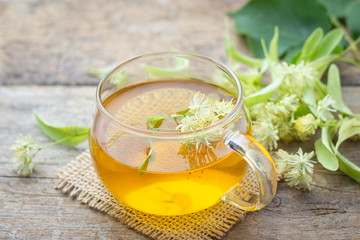 Cup of fresh herbal tea with blooming Tilia (linden, basswood) on wooden table.