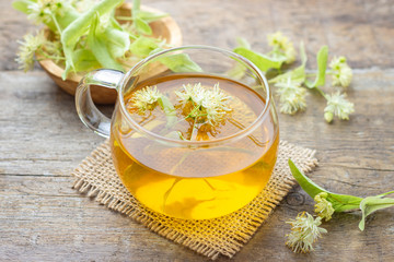 Cup of fresh herbal tea with blooming Tilia (linden, basswood) on wooden table.